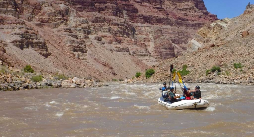A group of students in a raft raise their paddles into the air. 